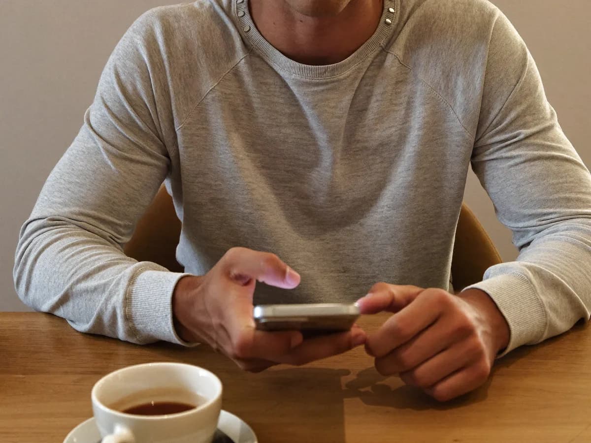 Man reviewing outfit combinations on phone, minimal wardrobe behind
